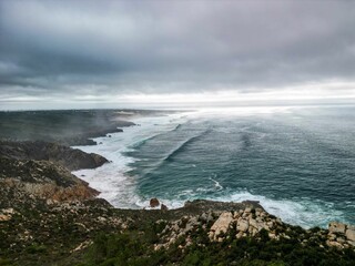 Drone shot over a cliff of Sintra-Cascais natural park by the sea under cloudy sky