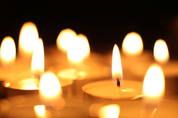 several burning warm candles or tealights close-up in the dark