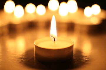 one tealight candle against a row of candles that are out of focus