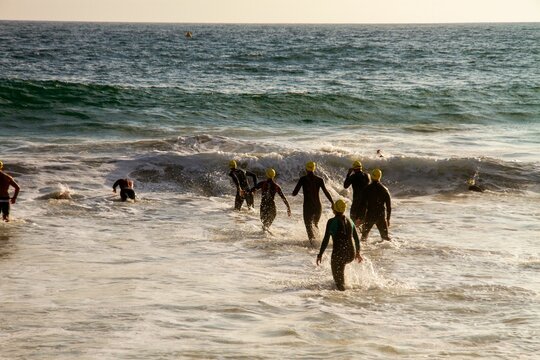 Rear Of A Group Of Competitive Swimmers Against The Sunlit Sea Waves Background