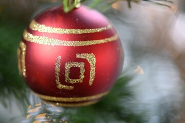 Closeup of a red bauble with golden lines hanging from Christmas tree blurred background
