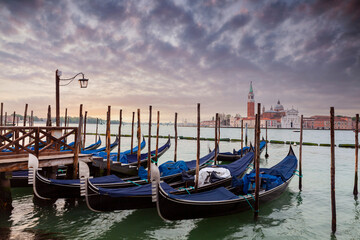 Naklejka premium A row of gondolas parked beside the Riva degli Schiavoni in Venice, Italy. View of the Venetian Lagoon. The Church of San Giorgio Maggiore on island of the Venice, Italy, Europe
