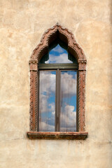 An old facade with a window with a reflection of the blue sky