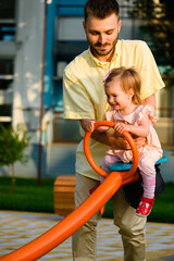 Father play with toddler girl at seesaw