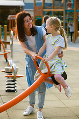 Mother and daughter play at playground seesaw