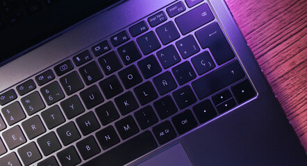 Desktop view of laptop keyboard with purple lights on wood table. Workplace. Work from home. Office desk.