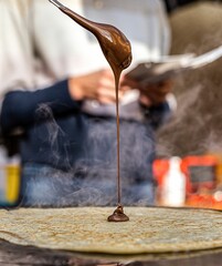 Vertical closeup of a spoon with chocolate pouring down to the hot blini