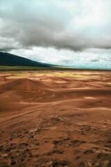 Sandy hill dunes with green mountains in a distance  under cloudy sunset sky, vertical shot