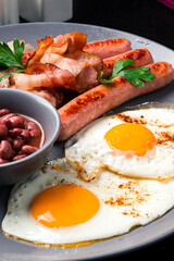 Full English Breakfast on dark table sausage eggs bean bacon tomatos mushroom