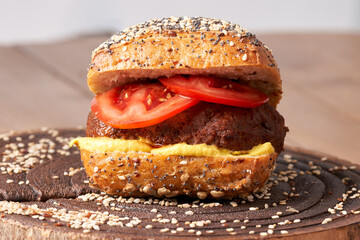 Homemade burger with tomatoes and mustard on the wooden table.