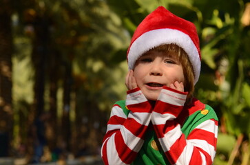 A boy in a Santa Claus hat on a background of palm trees. Concept: Christmas holidays, tropical resort, holidays with children. Winter holidays, gifts, travel