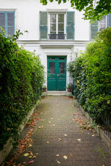 Vertical shot of an alley between green shrubs leading to green doors of a building