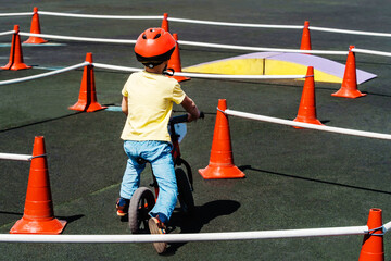 A child on a balance bike participates in competitions on the sports ground. Fenced area with...