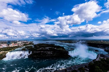 Aerial view of a beautiful rocky waterfall flowing downstream under a cloudy blue sky