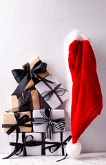 Boxes with wrapped  gifts  in black and white colors  and red Santas hat on white textured background. Place for text.