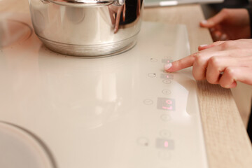 Female hand turns on electric hob closeup, finger presses sensor button on modern white induction...