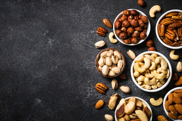 Nuts in the bowls. Cashew, hazelnuts, pecan, almonds, brazilian nuts and pistachios at black table. Top view with copy space.