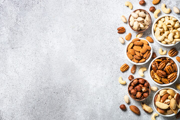 Obraz na płótnie Canvas Assortment of nuts in the bowls. Cashew, hazelnuts, pecan, almonds, brazilian nuts and pistachios at light stone table. Top view with copy space.