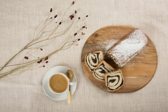 Top View Of A Sliced Swiss Roll And A Cup Of Cappuccino Served Over The Beige Fabric