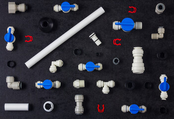 Top view photo of plastic plumbing, air product, pipe and tools. Valves, elbow and tee with locking clip on black background. Fitting industry