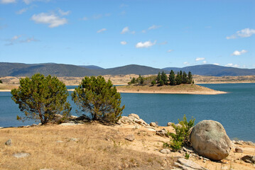 Jindabyne, New South Wales, Australia: View over Lake Jindabyne with trees and rocks in the foreground. Jindabyne is a tourist destination near the Snowy Mountains.