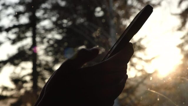 Millennial generation female scroll through news feed on app on phone. Close up of unrecognizable young woman using smartphone on background autumn sunset. Cinematic shot of girl at sunrise use phone