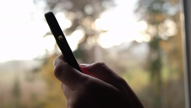 Close up unrecognizable young woman using smartphone on background autumn sunset. Millennial generation female scroll through news feed on app on phone. Cinematic shot of girl at sunrise use phone