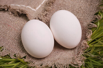 The chicken egg is white in color on burlap and on green grass.