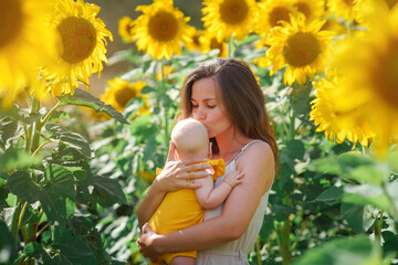 Young mother and baby girl happy together, hugging in nature in a field of yellow sunflowers. Concept of a happy family life