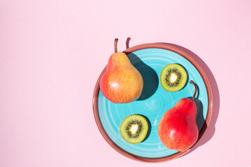 pears and kiwis lie on a blue plate on a pink background