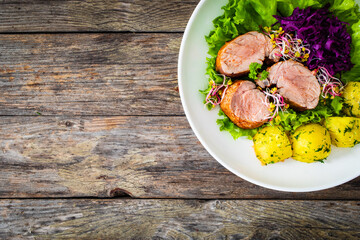 Fried pork loin with boiled potatoes and vegetables on wooden table
