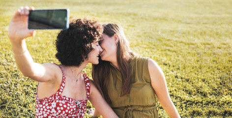 Some lesbian girls take a photo with their cell phones while kissing in an outdoor park.Save moments as a couple, have fun. LGTBI concept, copy space.