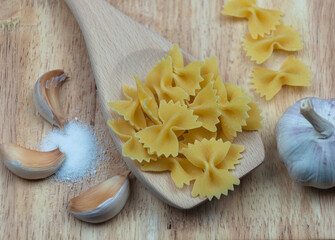 Pasta in the form of butterflies on a wooden board with garlic and salt close-up.