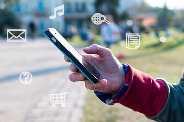 Hand with a smartphone outdoors and icons showing the variety of uses when connecting to the Internet.