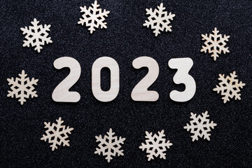 Fototapeta na wymiar New Year's card 2023. Wooden numbers of the year and snowflakes on a black shiny starry background. New Year greeting card template. Festive layout.