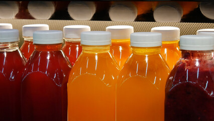Close-up of many beautiful plastic bottles of various natural juices in a cafe fridge shelf