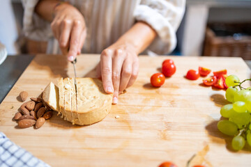 Female hands cutting slices of almond vegan cheese for breakfast