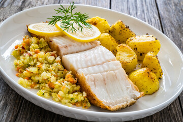 Fish dish - fried halibut with French fries and lemon on wooden table
