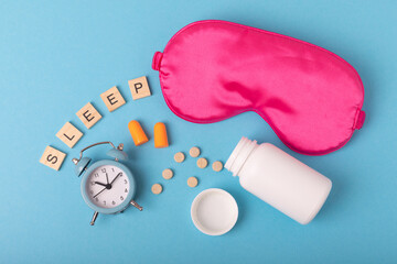 Sleeping mask, alarm clock, pills, ear plugs and the inscription SLEEP on a blue background. The...