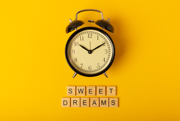Alarm clock and the inscription SWEET DREAMS on a yellow background. The concept of rest, sleep quality, good night, insomnia and relaxation. View from above. flat lay