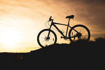 Fototapeta na wymiar silhouette of a bicycle standing on a hill, the background is an orange sky with blurry clouds
