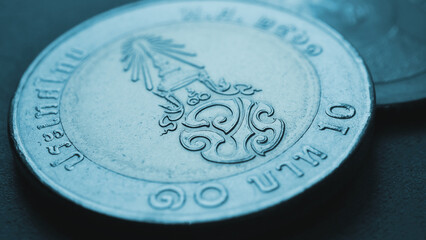 Translation: 10 baht Thailand. Thai coin pale blue wallpaper. Economy or finance. Loan and money. Savings and interest. Dark tinted background. Thai baht coin. King Maha Vajiralongkorn monogram. Macro