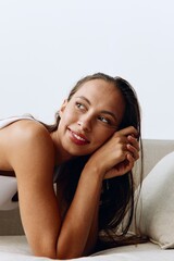 A woman lies relaxed on the couch and smiles looking at the camera in home clothes with long hair and tanned skin