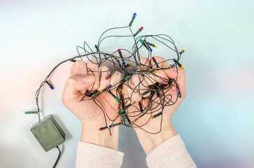 Women's hands hold tangled Christmas tree garland. Stress before celebration. old tree decorations