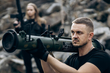 Guy and girl in military with bazooka and machine guns pose for camera