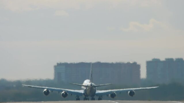 Widebody four-engine double-deck aircraft set to take off, rear view. Haze on the airport runway