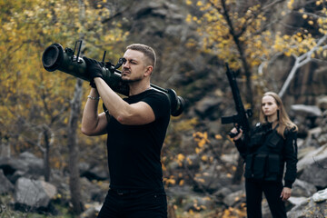 Guy and girl in military with bazooka and machine guns pose for camera