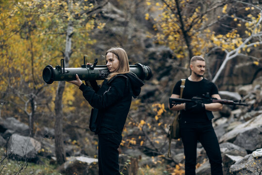 Guy and girl in military with bazooka and machine guns pose for camera