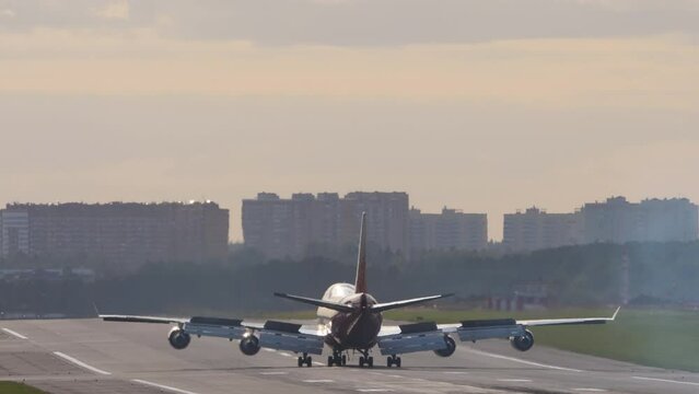 Widebody four-engine double-deck passenger aircraft braking after landing, rear view. Flaps up deceleration of the aircraft. Haze on the airport runway