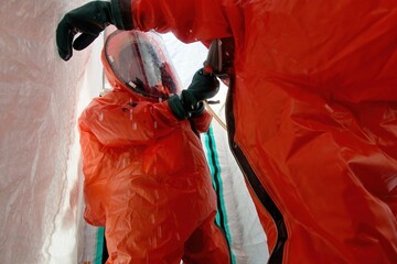 Firefighters in protective hazmat chemical suits carry out decontamination from a dangerous...